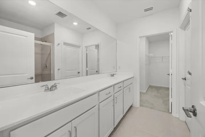 Dual vanity with white cabinetry and integrated sinks, oversized mirror, glass-enclosed shower, and tiled flooring