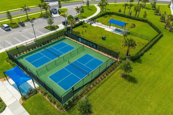 Two fenced pickleball courts, adjacent fenced green space, and a paved parking area