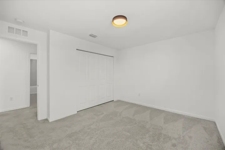 Neutral wall paint, ceiling-mounted light fixture, white bi-fold closet doors, and light gray patterned carpeting
