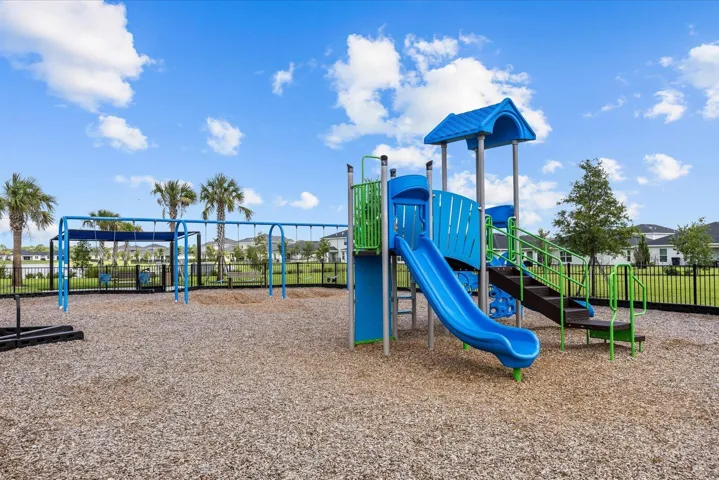 Community playground featuring a multi-level play structure, slide, swing set, and protective wood chip surfacing