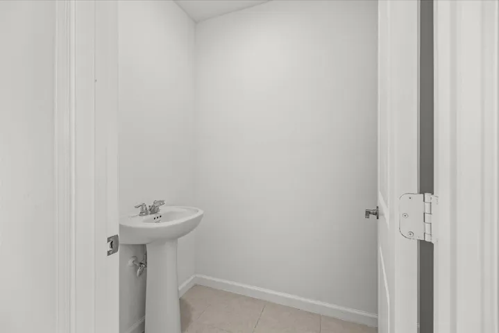 Pedestal sink with chrome faucet, light-toned flooring, and white walls