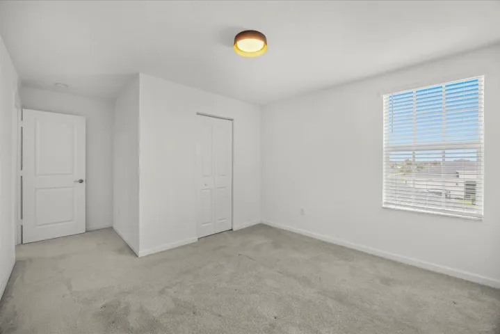 Neutral tone wall color, carpet flooring, a window with horizontal blinds, and a bi-fold closet door