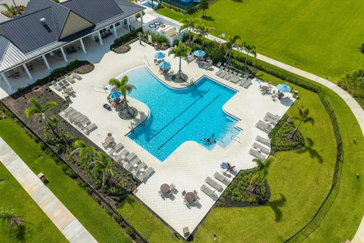 Resort-style pool with integrated lap lane, expansive sun deck, multiple shaded lounge areas, and surrounding landscaped grounds