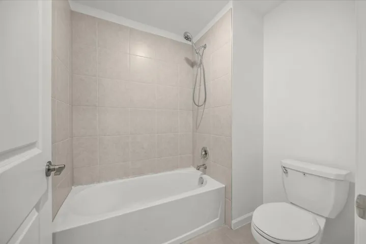 Bathtub with tiled surround, showerhead, and a white toilet