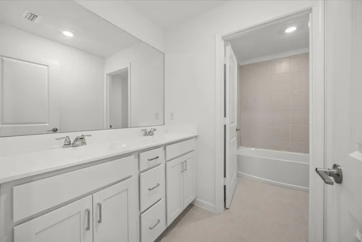 Dual vanity with white cabinetry and chrome fixtures, large rectangular mirror, and light tile flooring