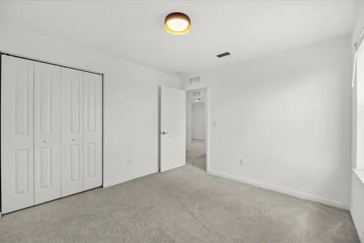 Neutral wall paint, light gray carpet, white bi-fold closet doors, and a ceiling-mounted light fixture