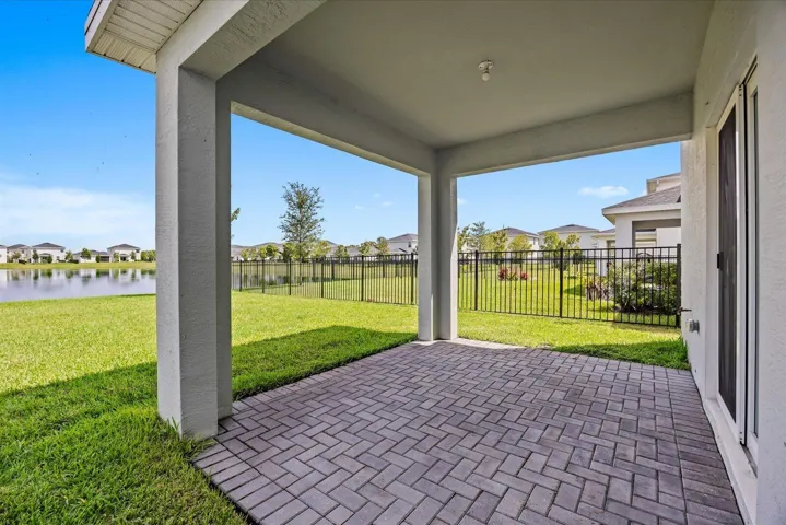 Covered patio with paver flooring, leading to a fenced yard with a water feature