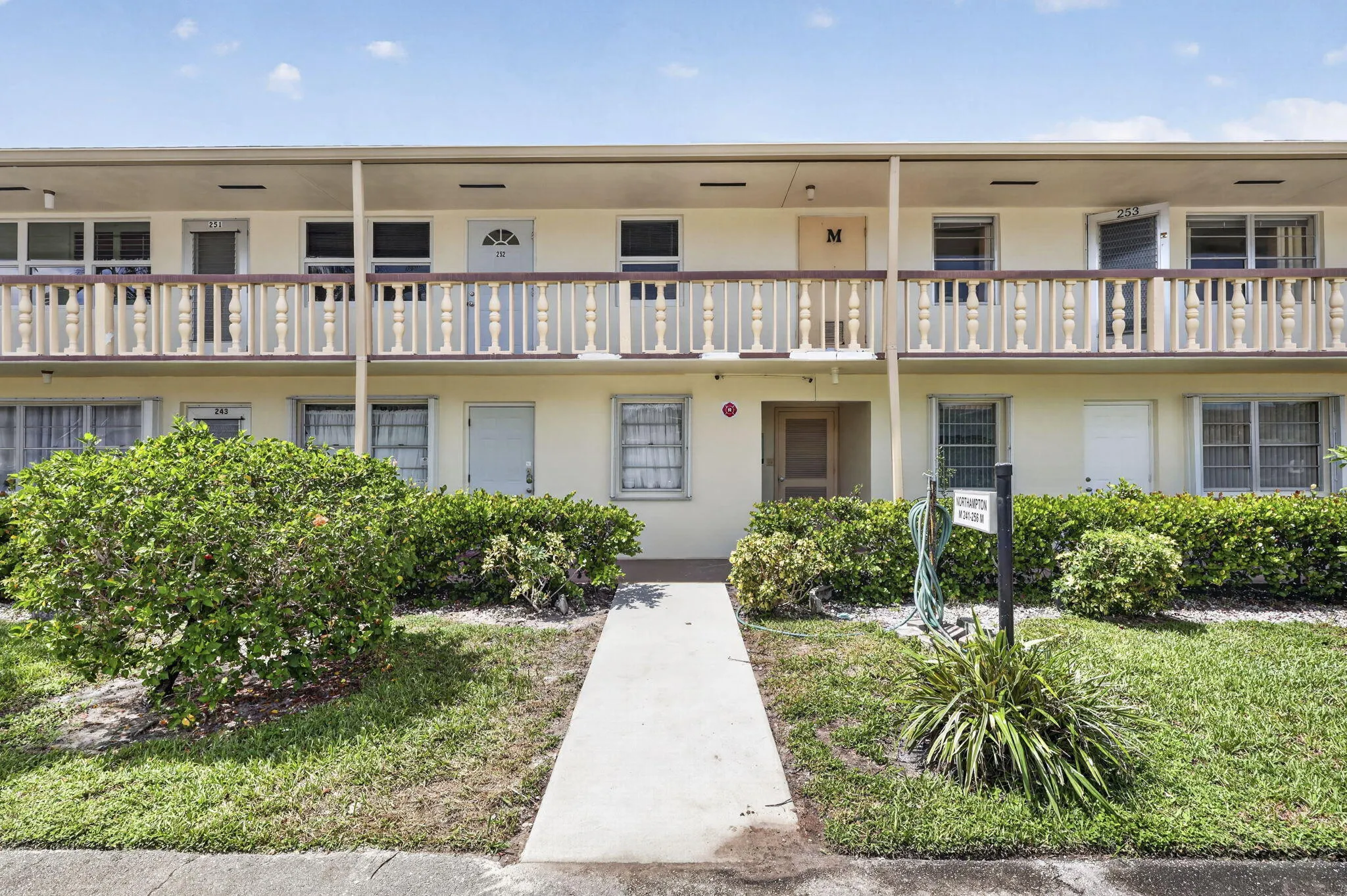 Two-story building exterior with a light-colored stucco finish, individual entry doors, and ground-level plantings