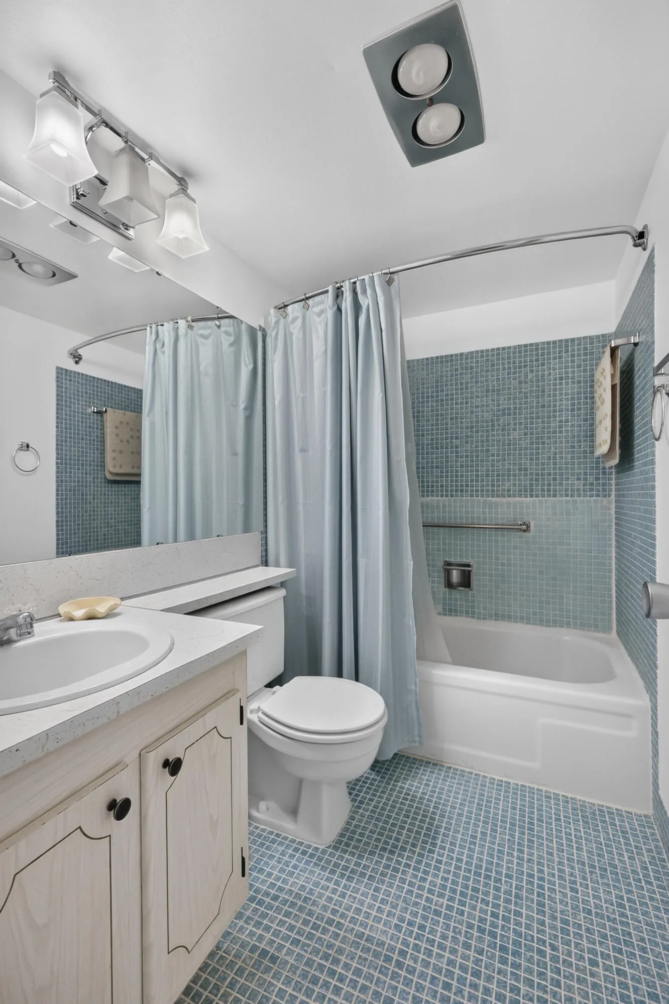 Bathroom featuring a white vanity with integrated sink, toilet, tub with blue mosaic tile surround, and blue patterned floor tile