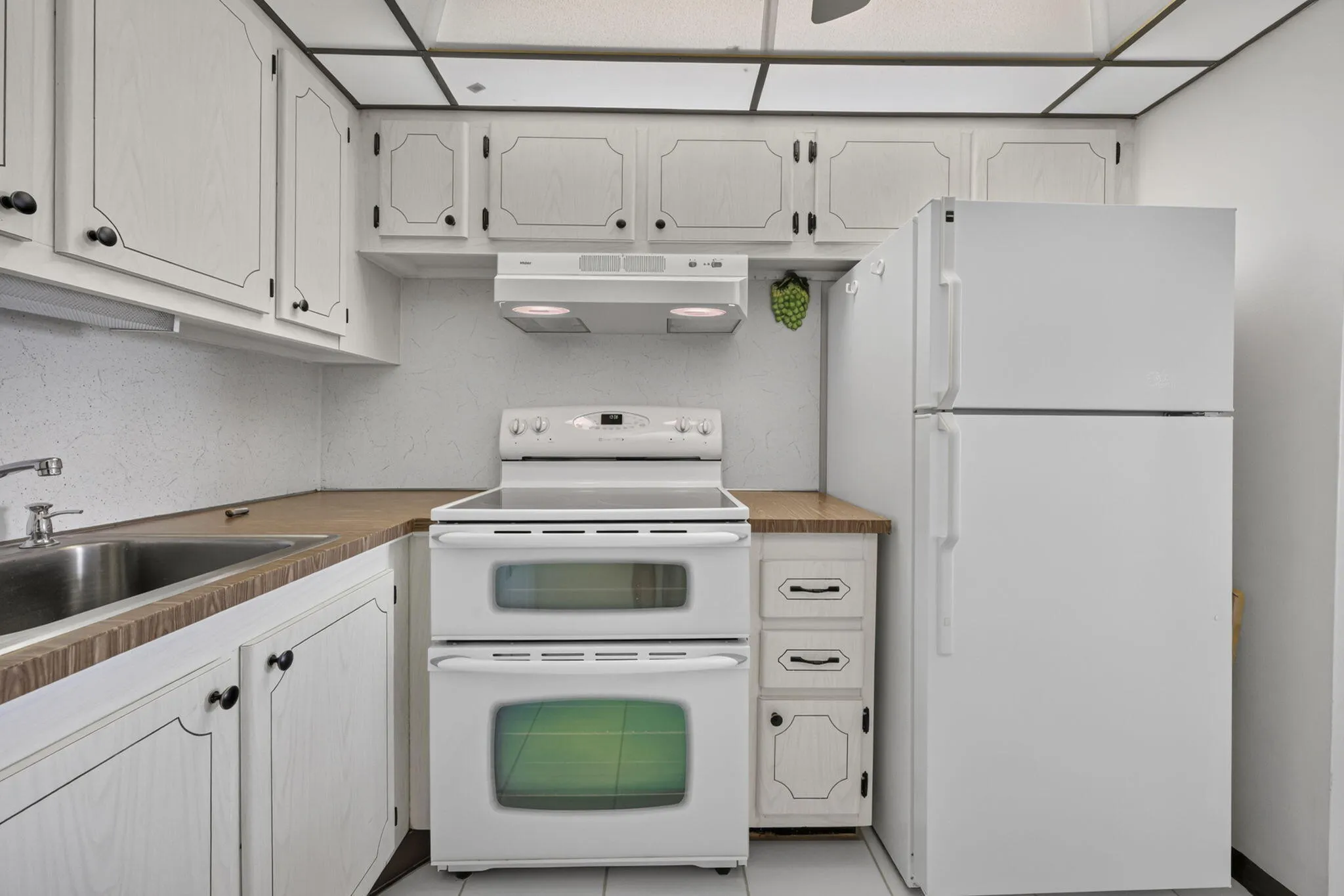 White cabinetry with black hardware, wood-finish countertops, stainless steel sink, white electric range with double oven, and white refrigerator