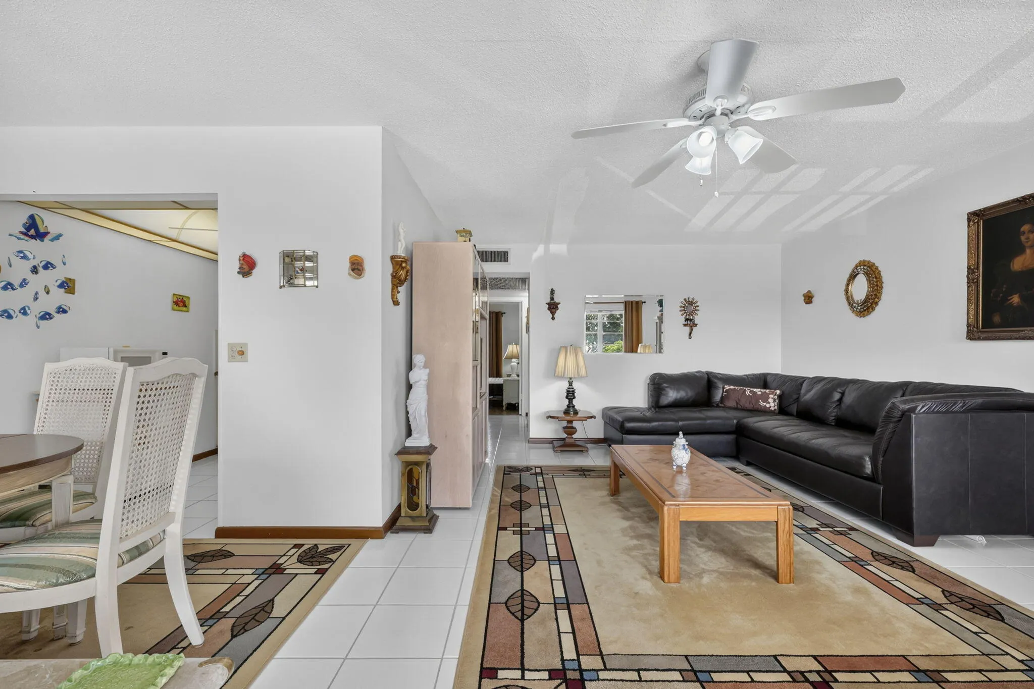 Spacious living area featuring white tile flooring, ceiling fan with integrated lighting, and white walls