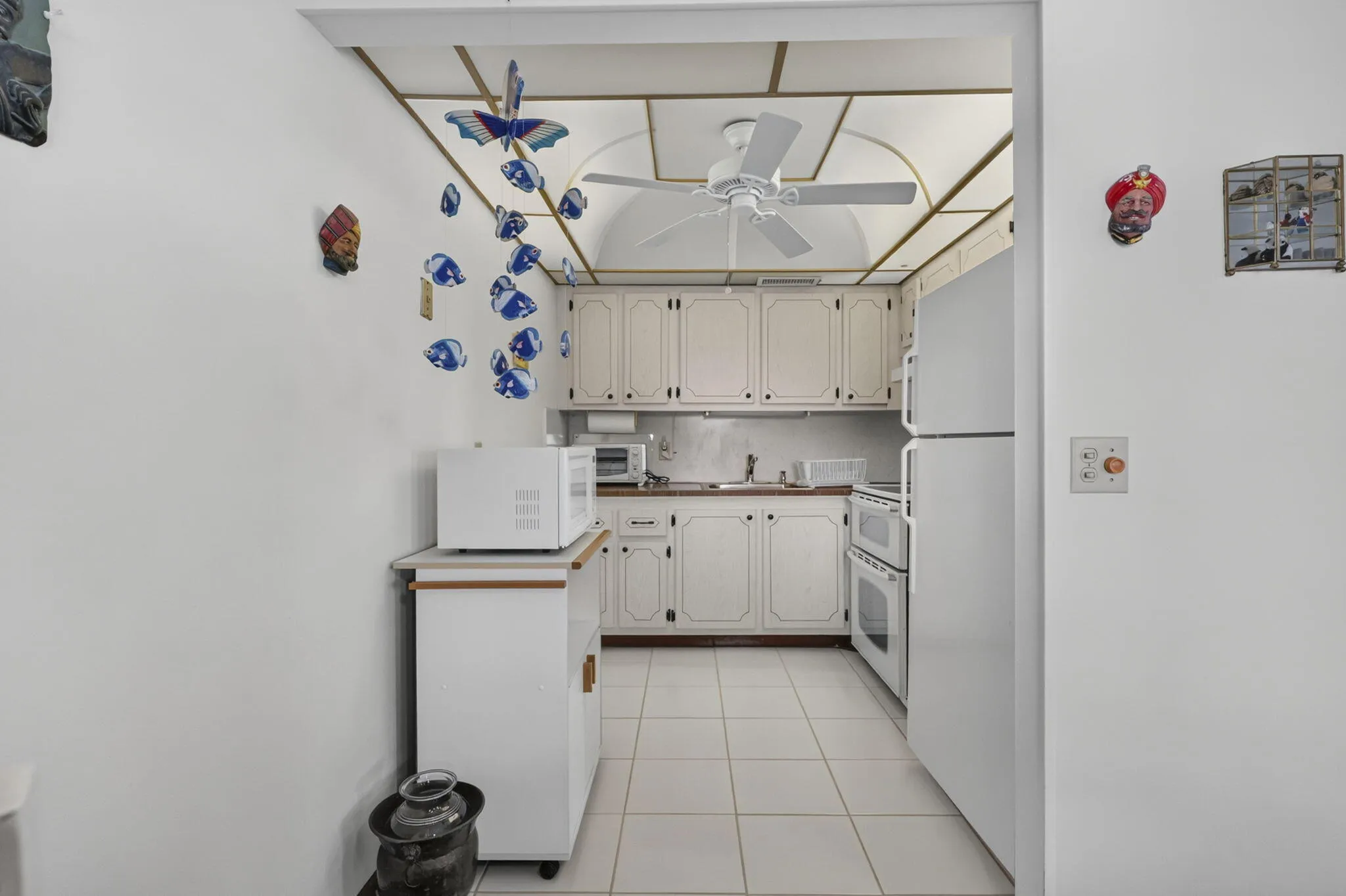 Galley kitchen with white cabinetry, tile flooring, white appliances, and a ceiling fan