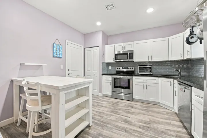 White shaker cabinetry with stainless steel appliances, dark countertops, and a subway tile backsplash