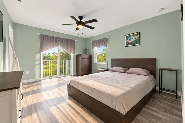 Wood-finish flooring, ceiling fan with integrated lighting, glass sliding door with balcony access, and natural light