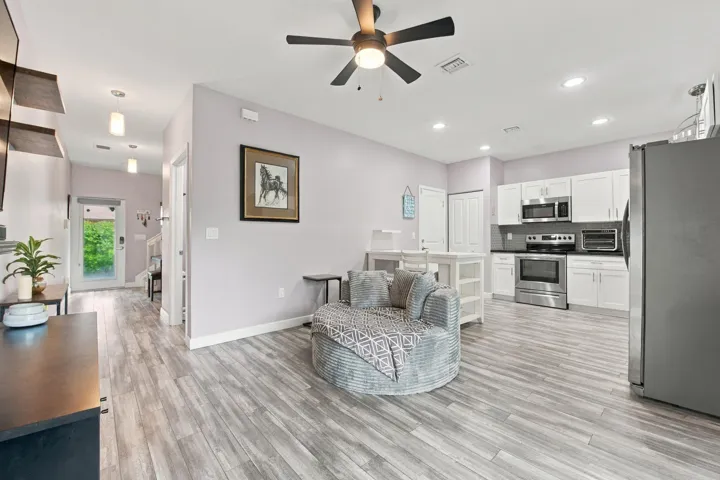 Open-concept living area with wood-finish flooring, white cabinetry, stainless steel appliances, and recessed lighting