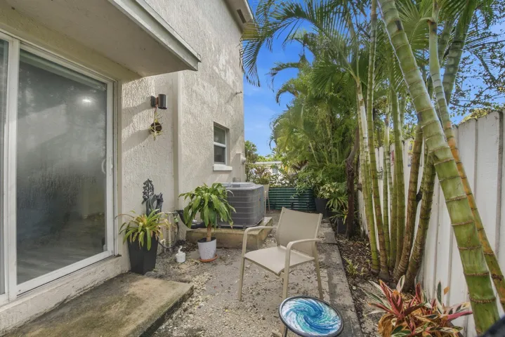 Private outdoor patio space featuring a stucco exterior, sliding glass door, mature palm trees, and a privacy fence