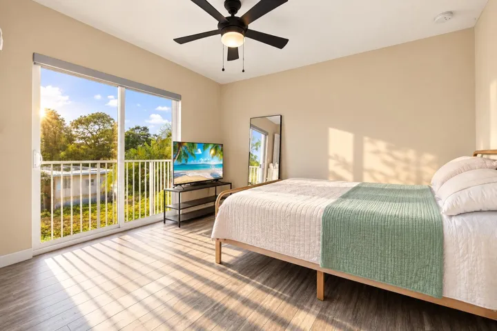 Sliding glass doors opening to a private balcony, wood-finish flooring, neutral wall tones, and a ceiling fan with integrated lighting