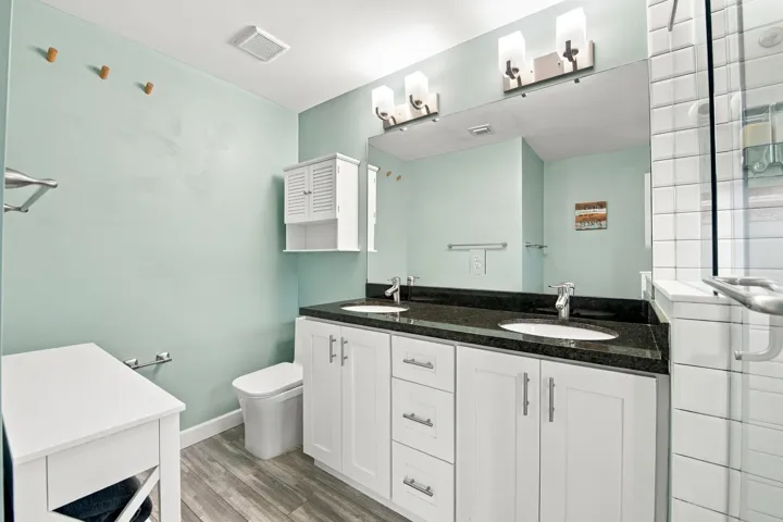 Dual vanity with dark stone countertop, white shaker cabinetry, and integrated sinks