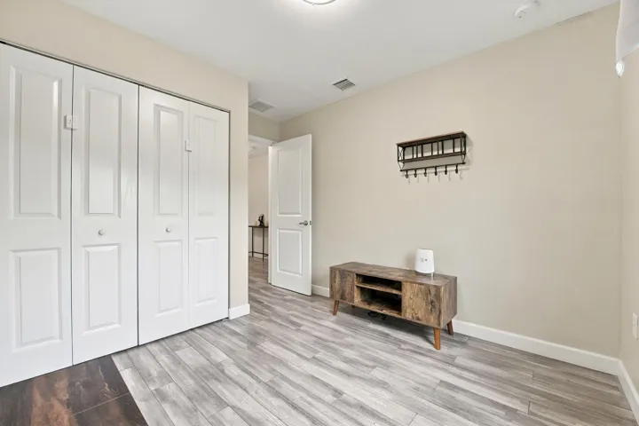 Neutral wall color, wood-finish flooring, white bi-fold closet doors, white baseboards, and a white interior door with a silver-tone knob