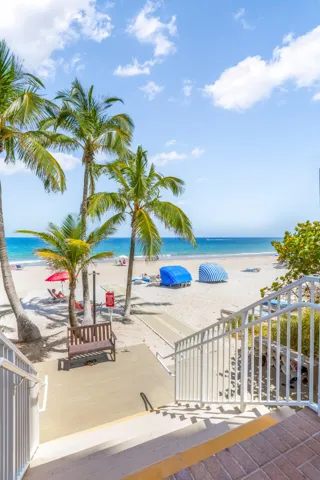 Direct beach access with a wide sandy expanse, mature palm trees, and ocean waters