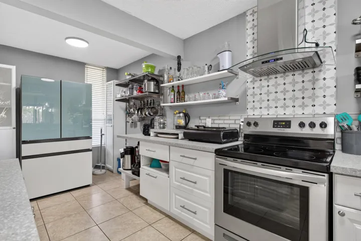Contemporary kitchen featuring a stainless steel range, patterned tile backsplash, white cabinetry, and a neutral tile floor
