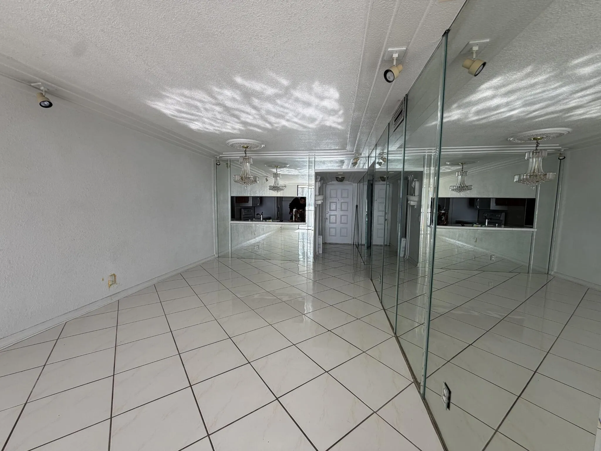 White tile flooring, full-height mirrored wall, crown molding, and two ceiling-mounted light fixtures