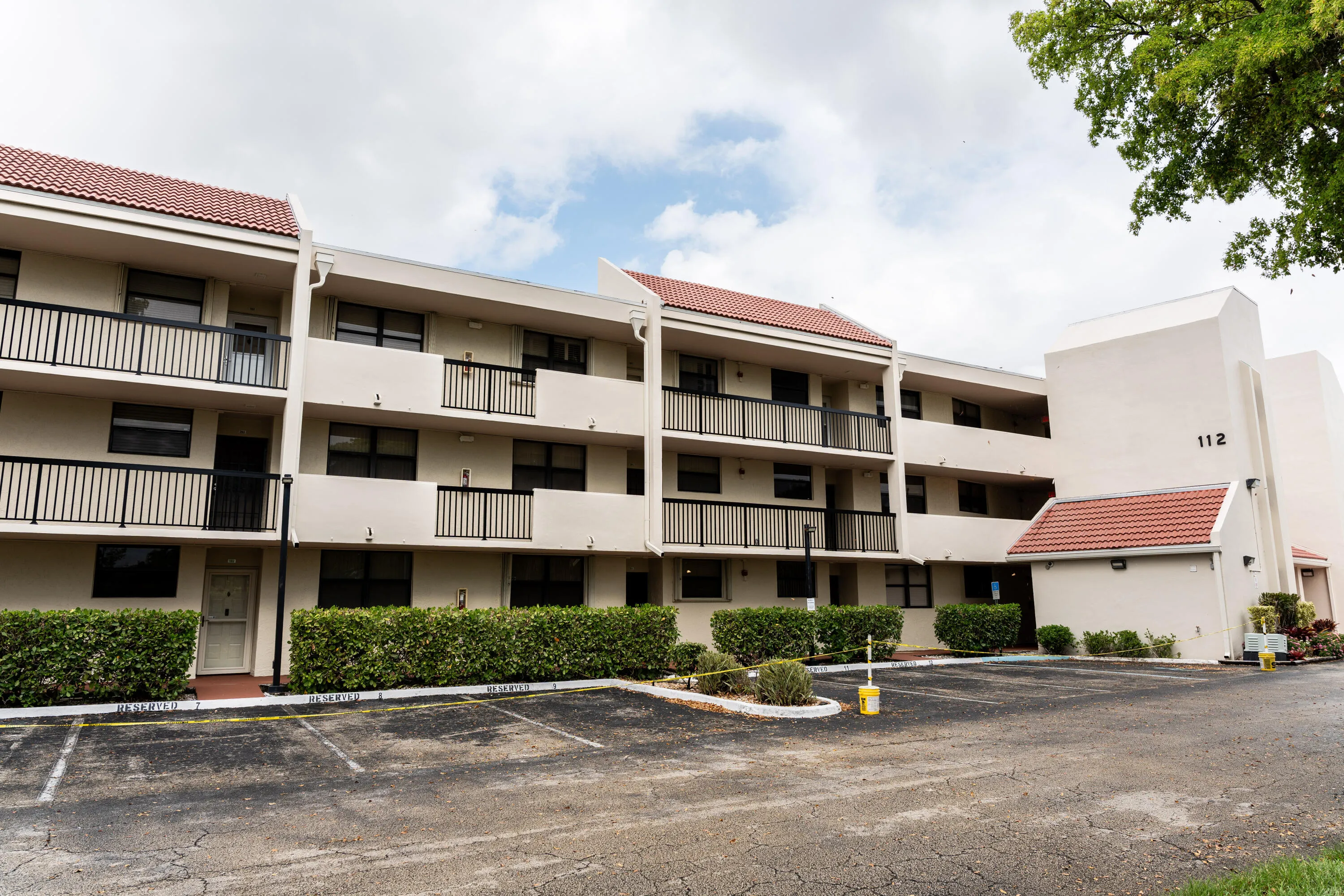 Multi-story building featuring tile roofing, multiple balconies with black railings, and a stucco exterior finish