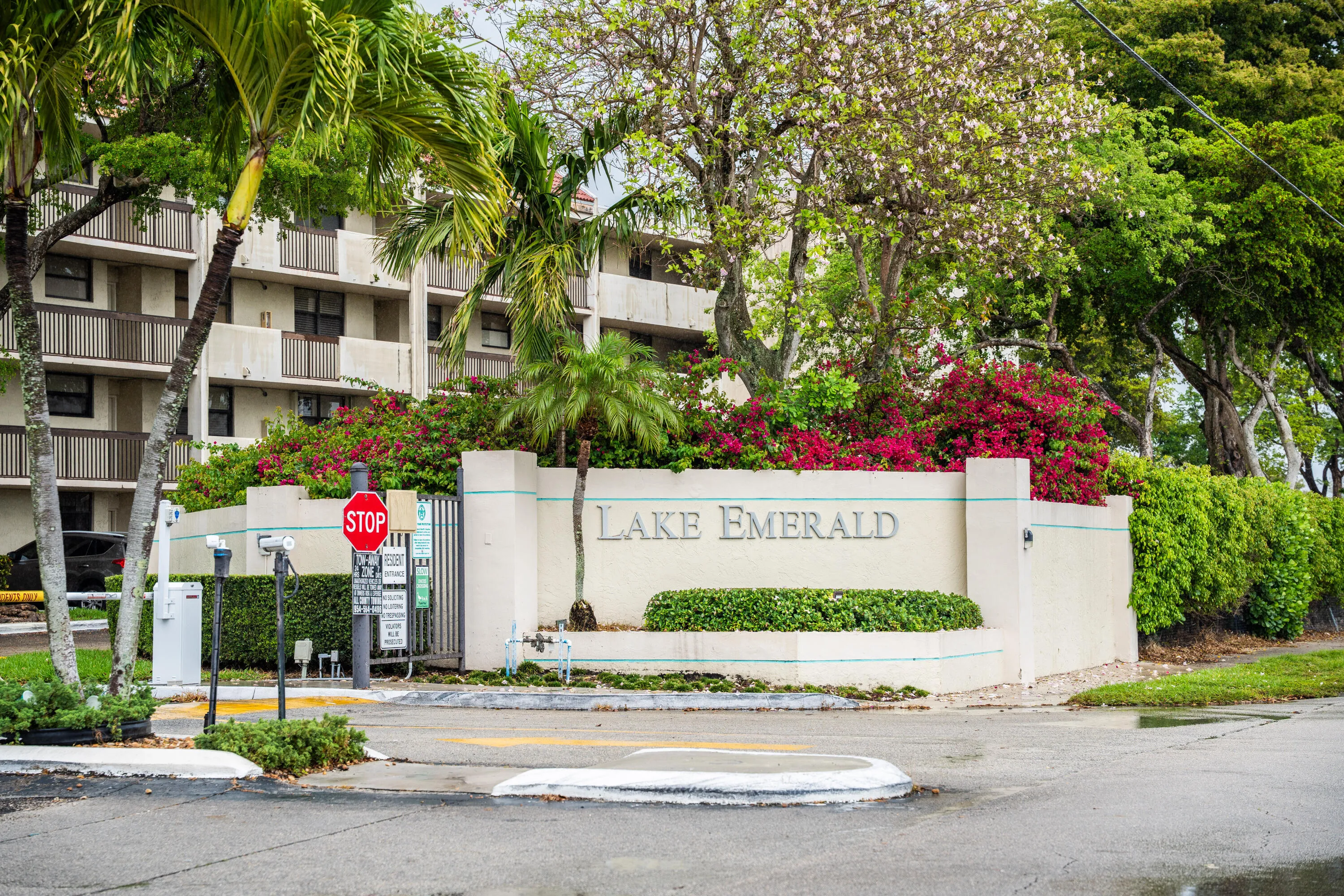 Entryway signage with "LAKE EMERALD" inscription, bordered by lush landscaping and a security gate
