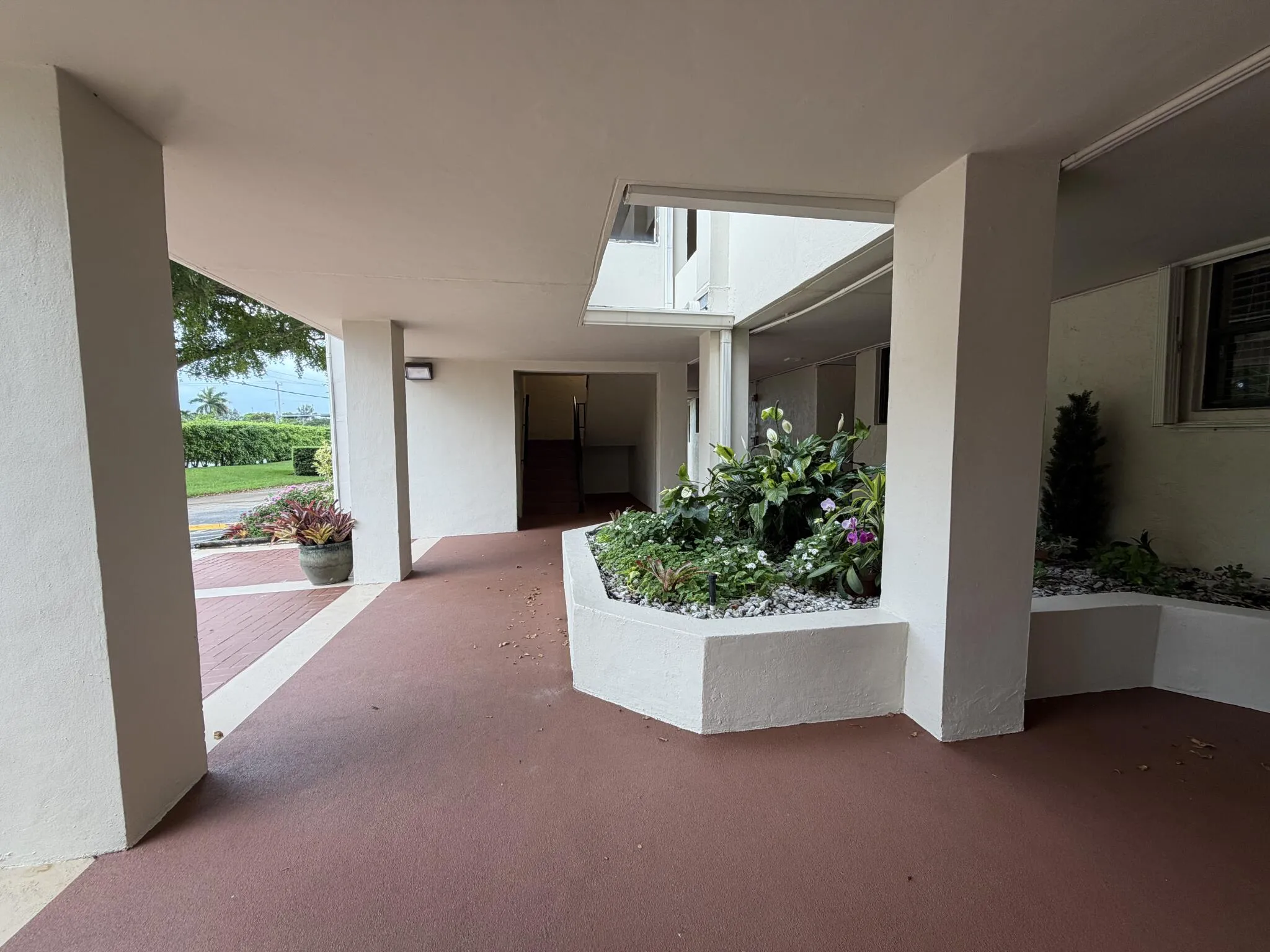Covered walkway with a planter, concrete pillars, and a brown-toned floor