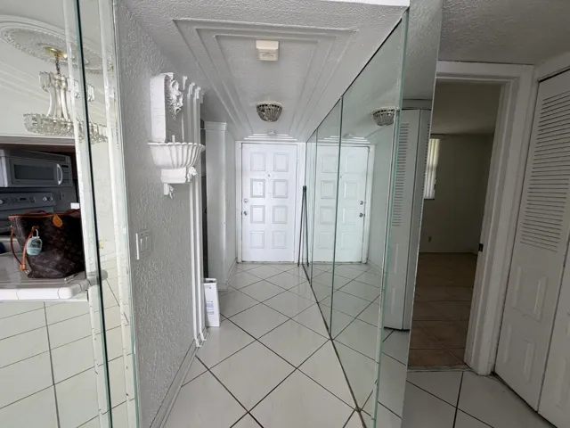 Mirrored hallway walls, recessed ceiling panels, decorative ceiling medallions, tiled flooring, and a paneled entry door