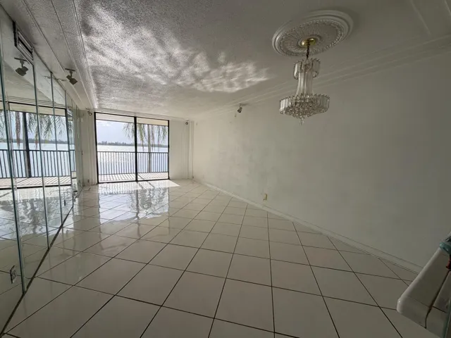 Sliding glass doors with a water backdrop, tiled flooring, mirrored wall, ceiling-mounted crystal chandelier, and ceiling crown molding