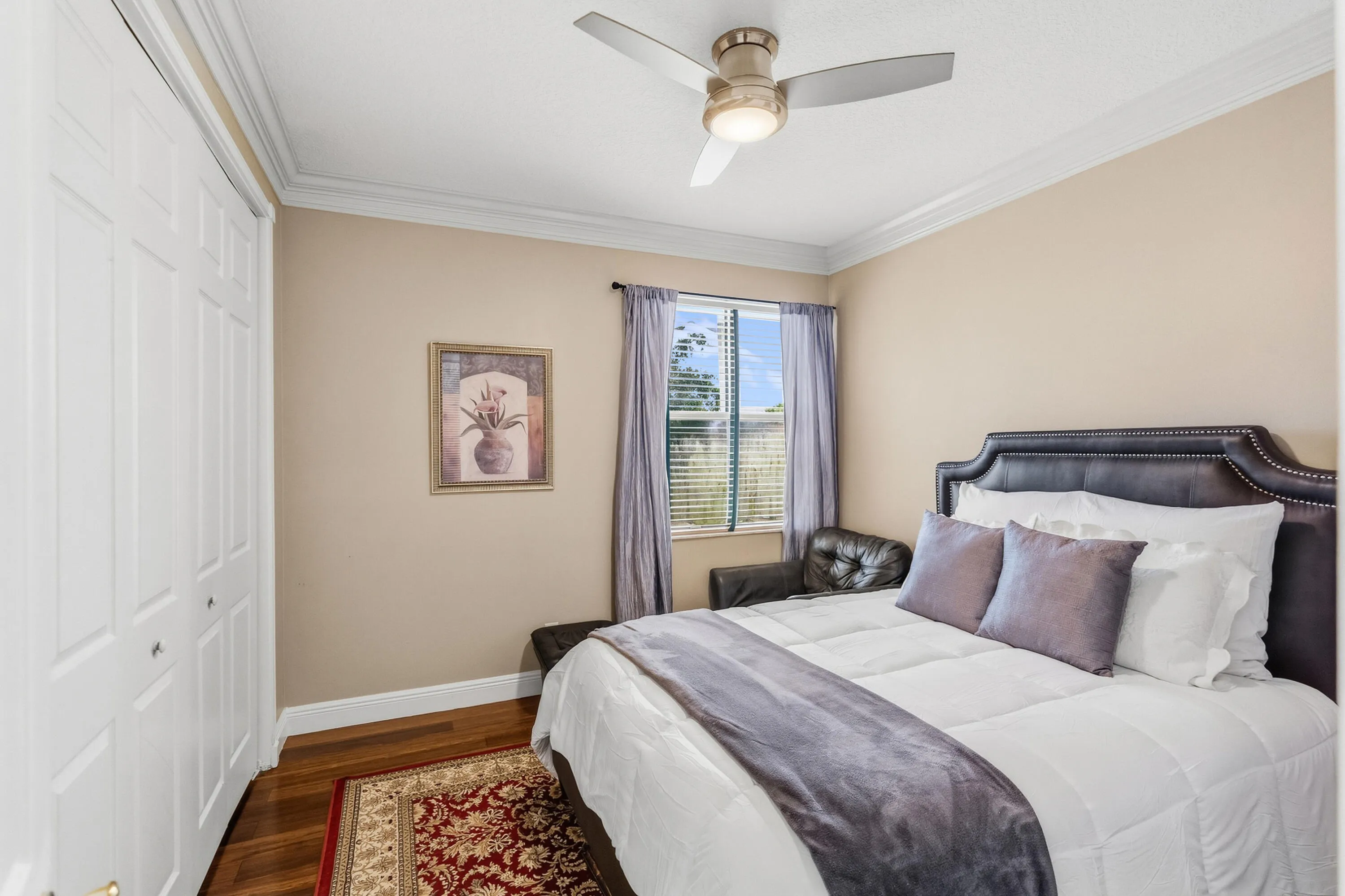 Comfortable upstairs bedroom with wood flooring, crown molding, closet space and room for a queen-size bed.