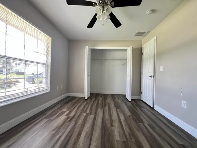 Wood-finish flooring, ceiling fan with light fixture, window with blinds, and a built-in closet with shelving