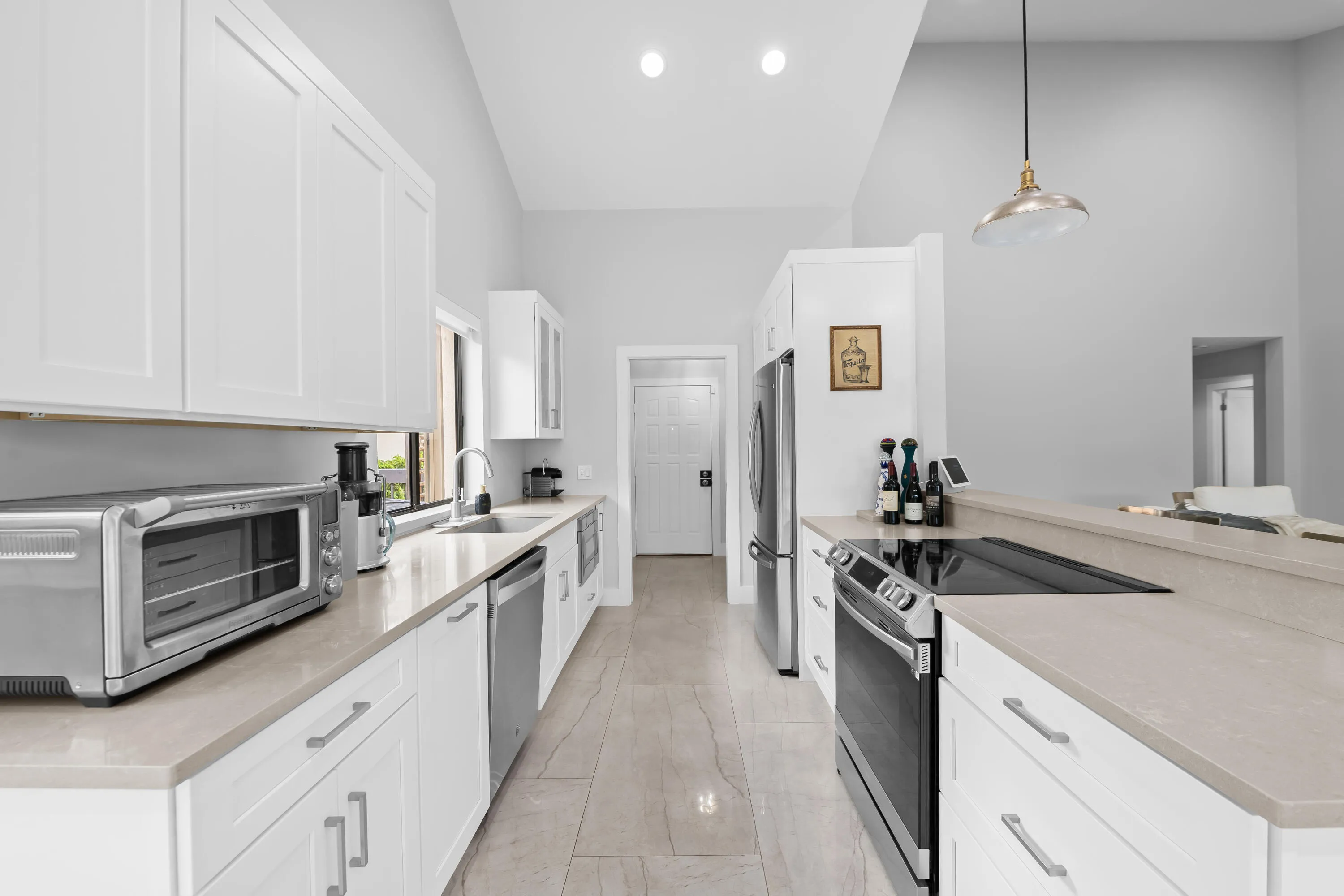 Contemporary kitchen featuring white cabinetry, light-toned countertops, stainless steel appliances, and a vaulted ceiling with recessed lighting