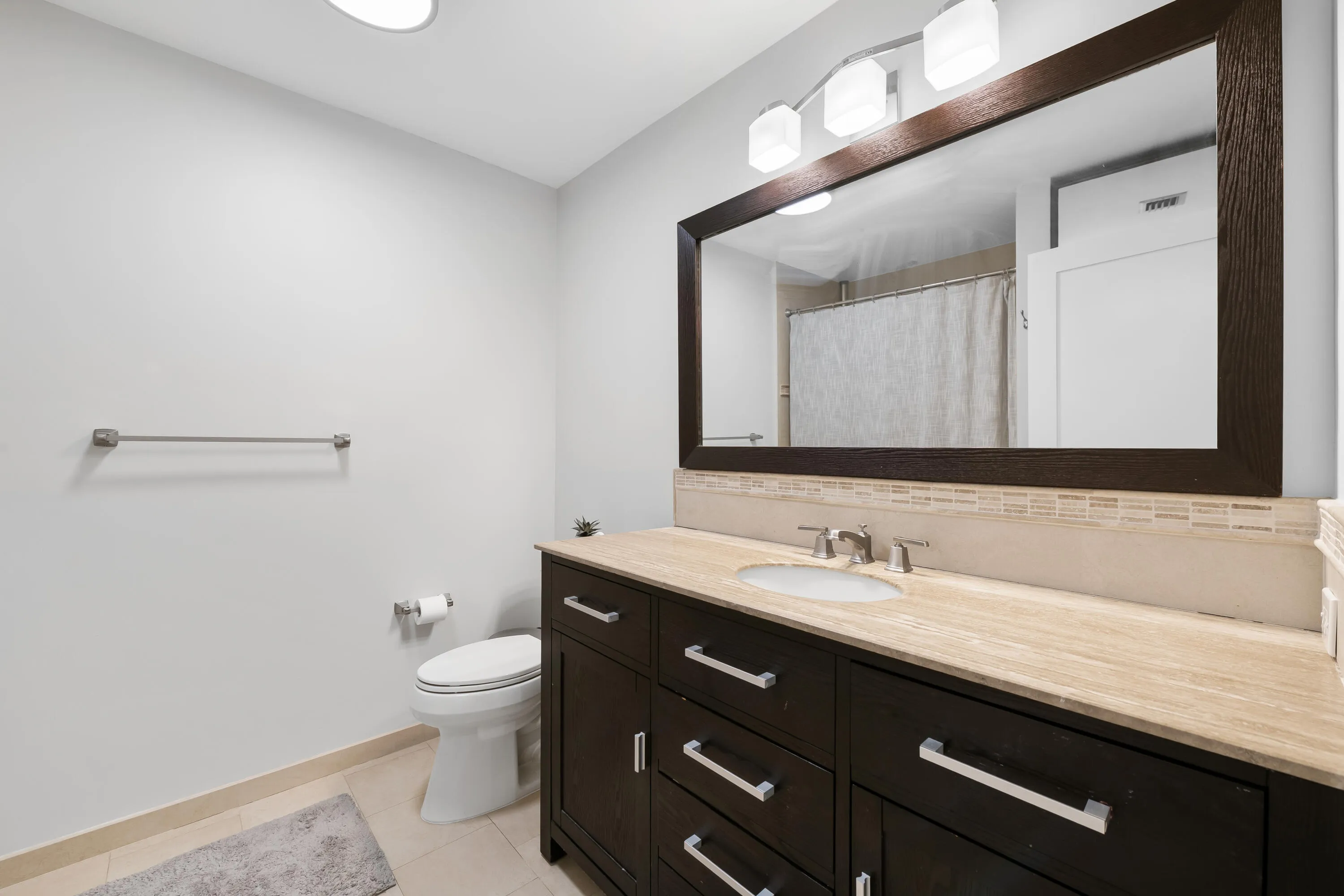 Dark wood-finish vanity with a light-toned countertop, undermount sink, and brushed nickel faucet