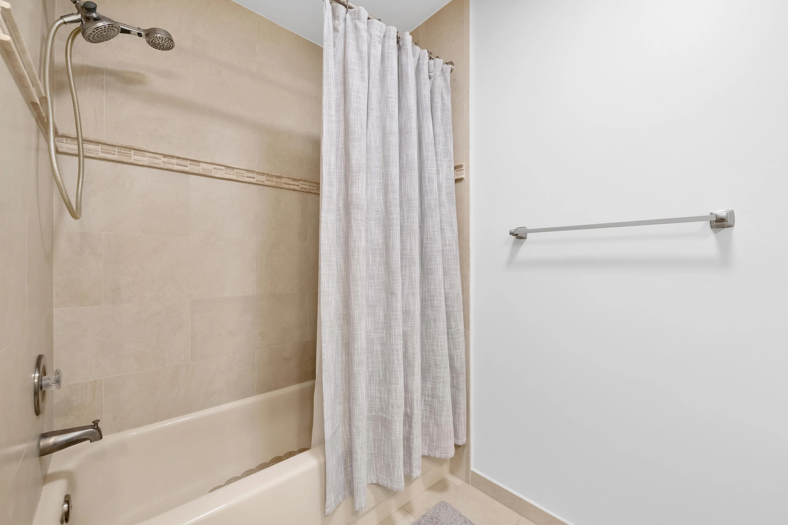 Bathtub with brushed nickel fixtures, tiled surround featuring an accent band, and a dual-head shower system