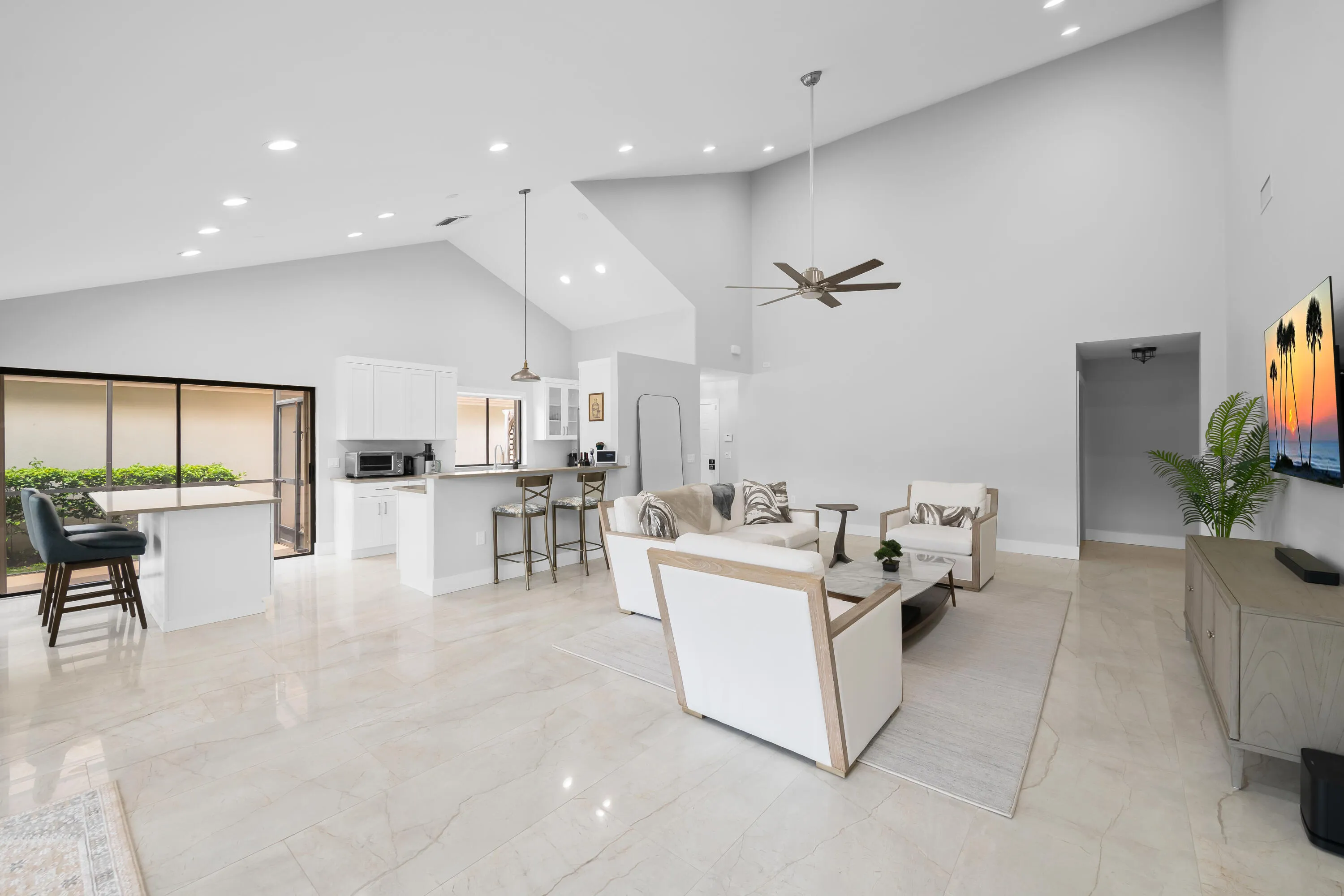 Vaulted ceilings with recessed lighting, polished tile flooring, kitchen island with breakfast bar, white cabinetry, and sliding glass doors