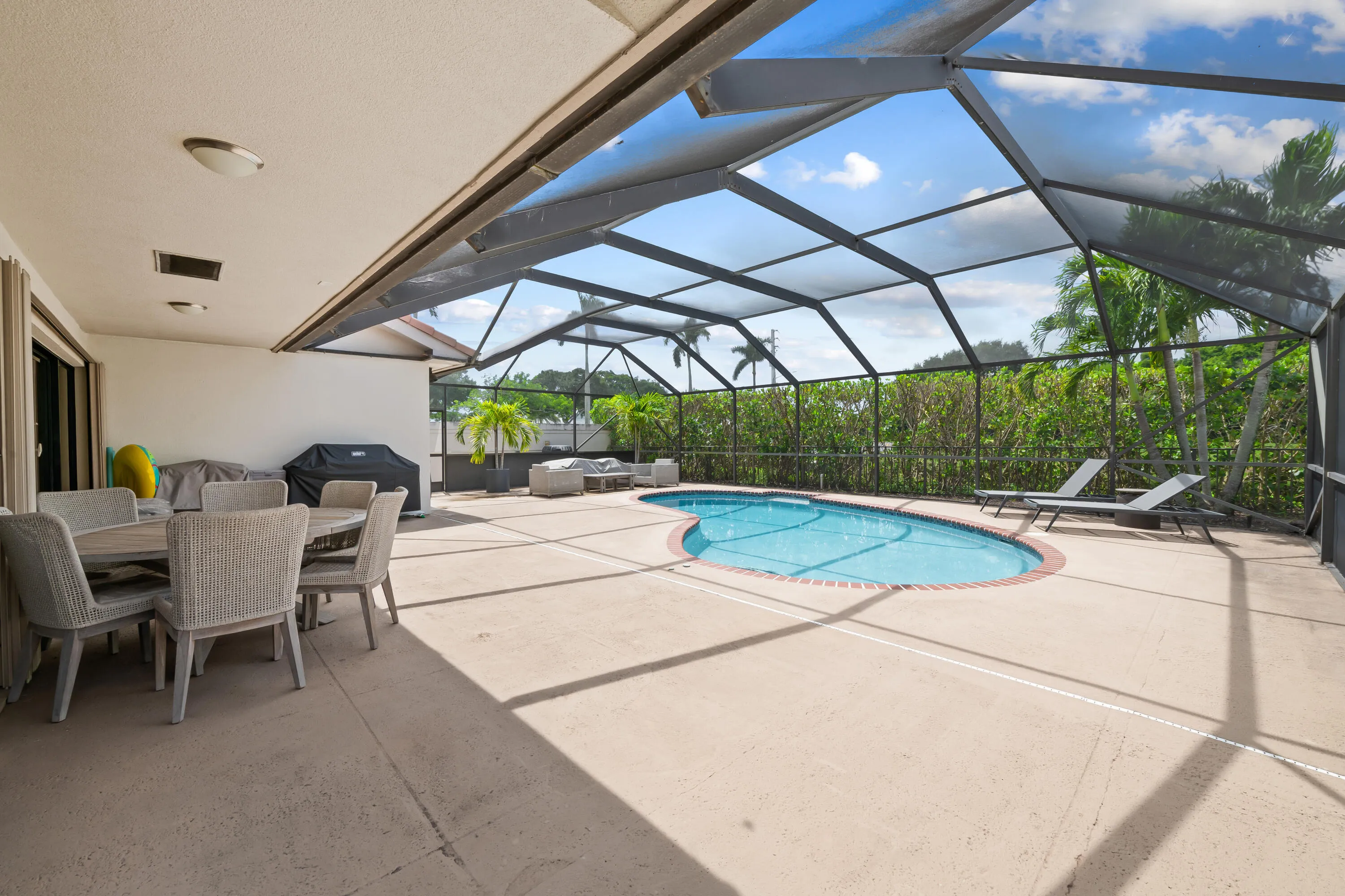 Screened-in pool area featuring a freeform pool, expansive concrete patio, and a covered lanai