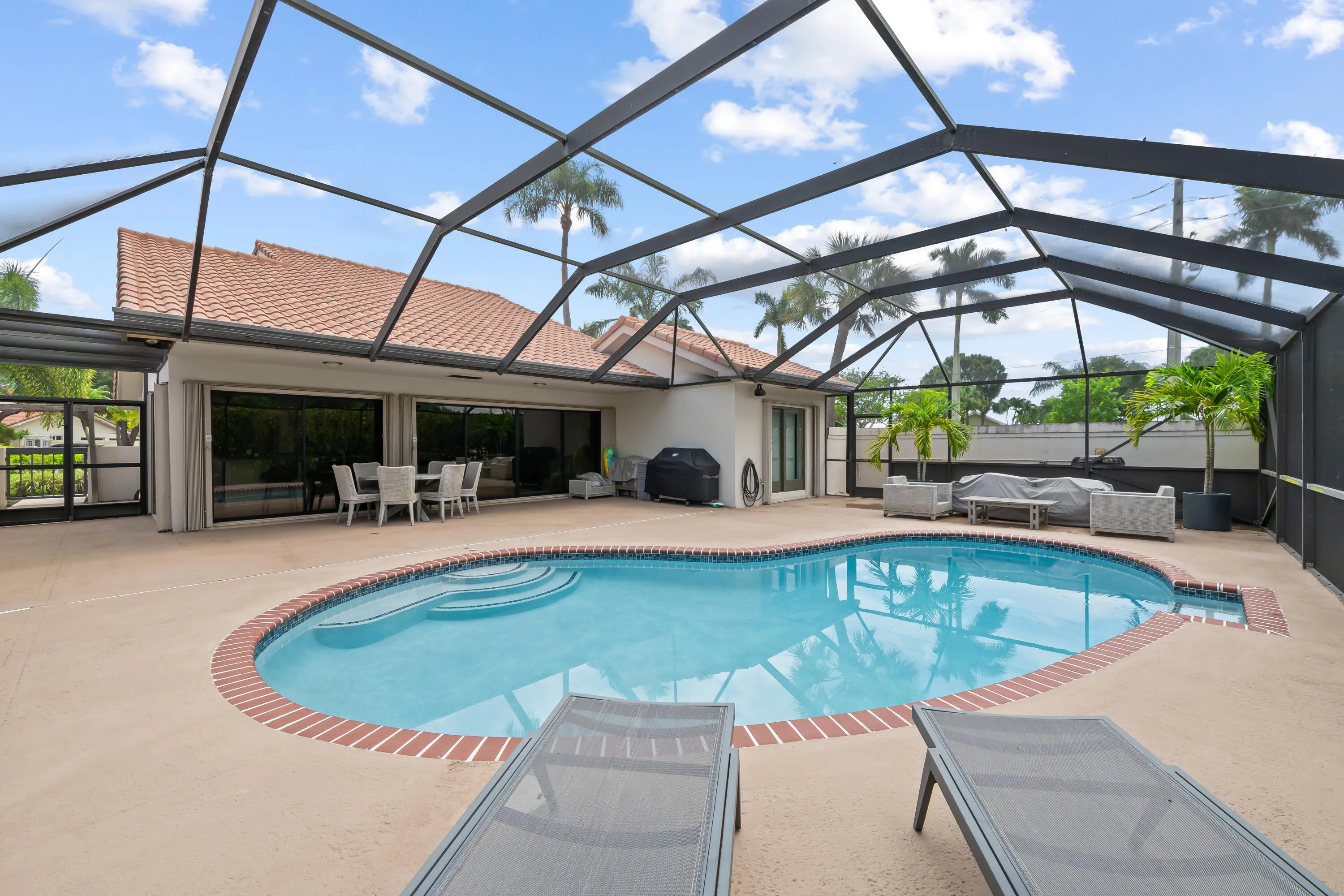 Screened-in swimming pool with brick coping, expansive concrete decking, and direct access to interior spaces through large sliding glass doors