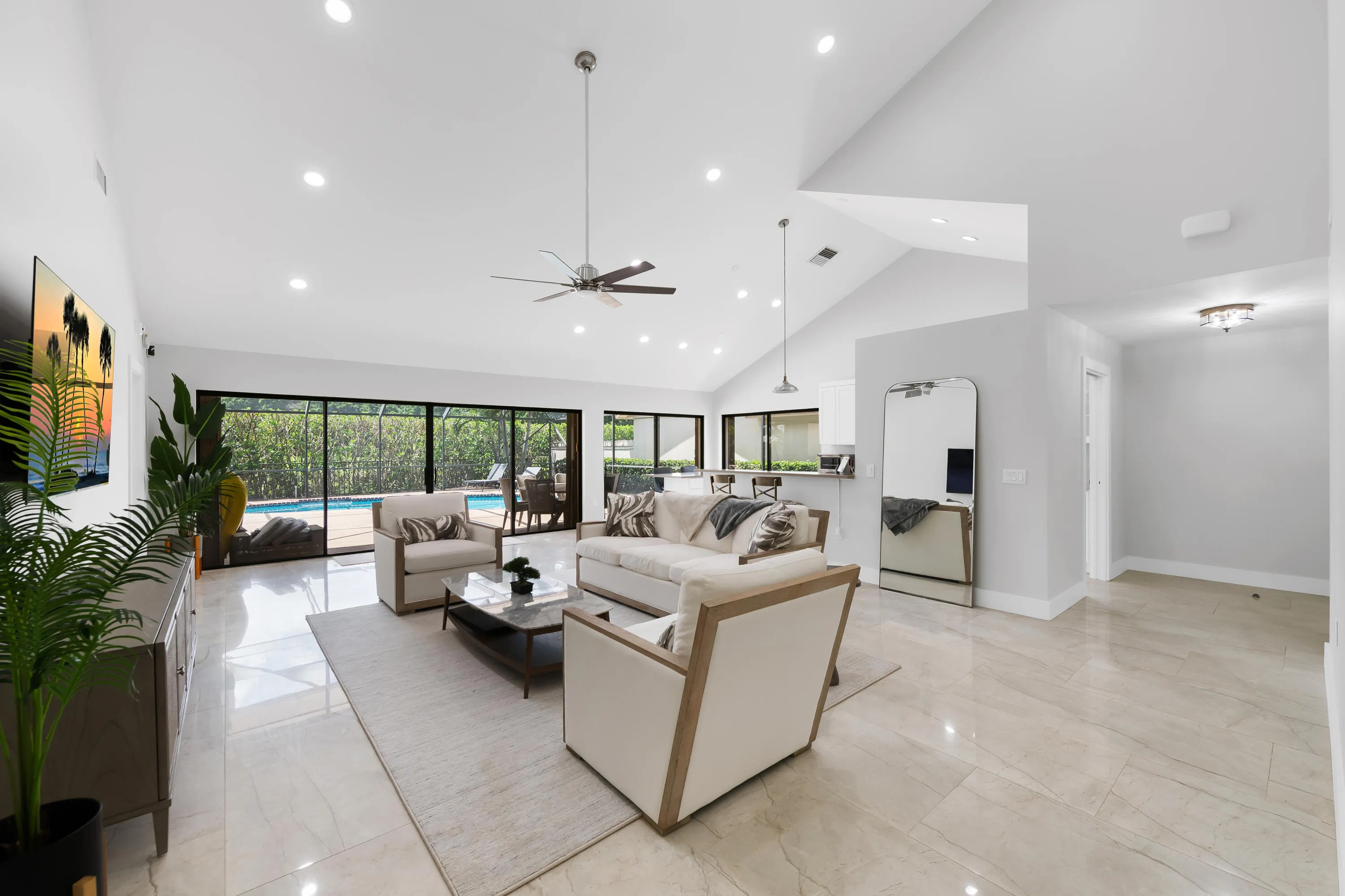 Vaulted ceilings, recessed lighting, polished tile flooring, ceiling fan, and extensive sliding glass doors leading to a screened lanai with a pool