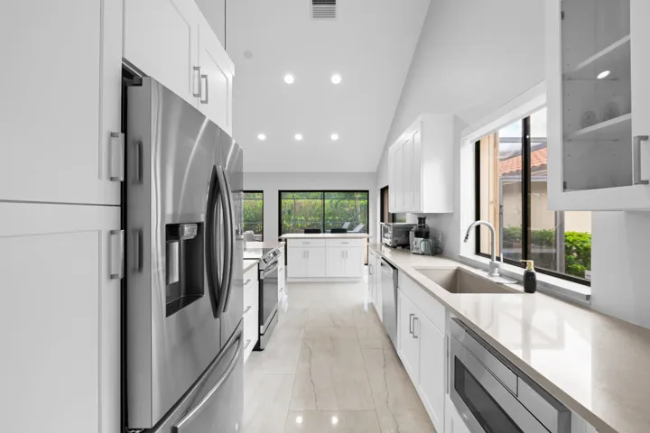 Bright kitchen featuring vaulted ceilings, recessed lighting, white cabinetry, stainless steel appliances, and a window over the sink