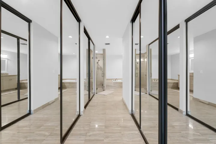 Hallway with mirrored closet doors, tiled flooring, recessed lighting, and a partial bathroom featuring a built-in tub