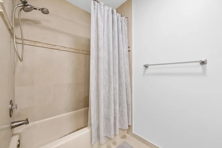 Bathtub with brushed nickel fixtures, tiled surround featuring an accent band, and a dual-head shower system