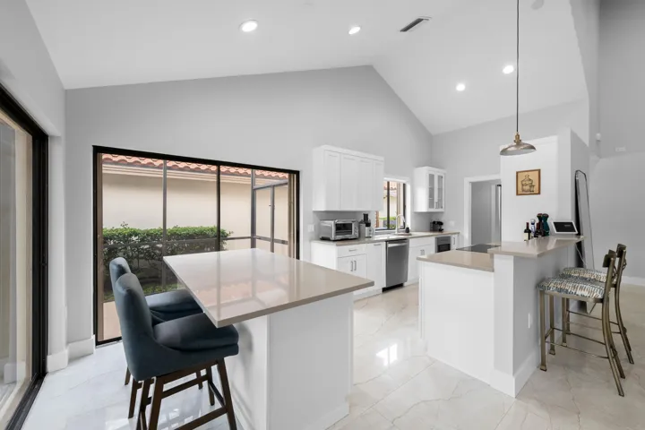 Vaulted ceiling, recessed lighting, white cabinetry, stainless steel appliances, and large format floor tiling