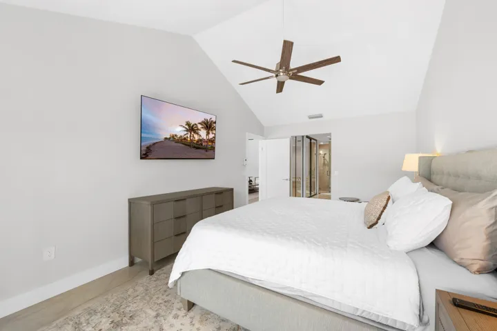 Vaulted ceiling with a ceiling fan, wall-mounted television, wood-finish flooring, and a built-in closet with sliding glass doors