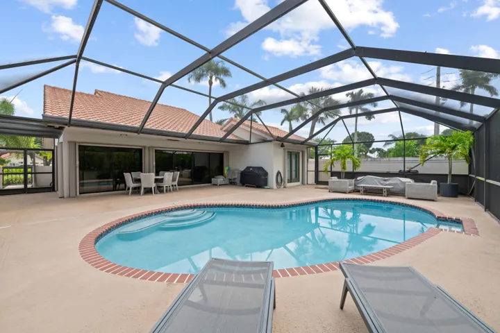 Screened-in swimming pool with brick coping, expansive concrete decking, and direct access to interior spaces through large sliding glass doors