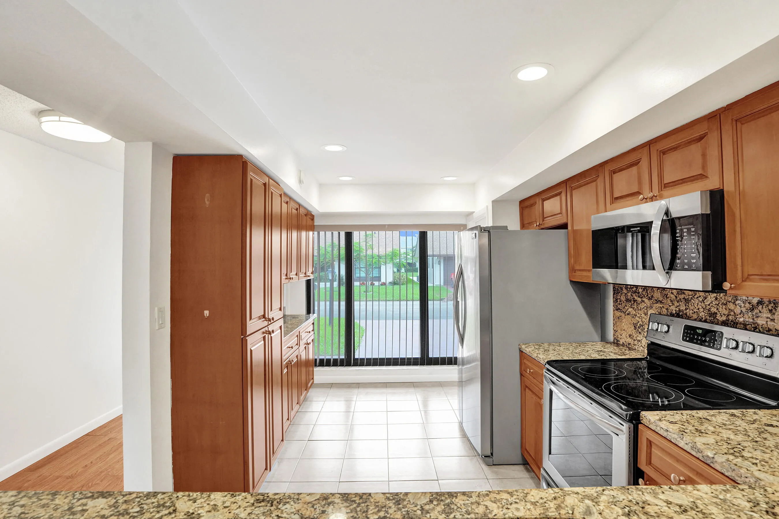 Kitchen featuring wood cabinetry, stainless steel appliances, tiled flooring, granite countertops, and recessed lighting