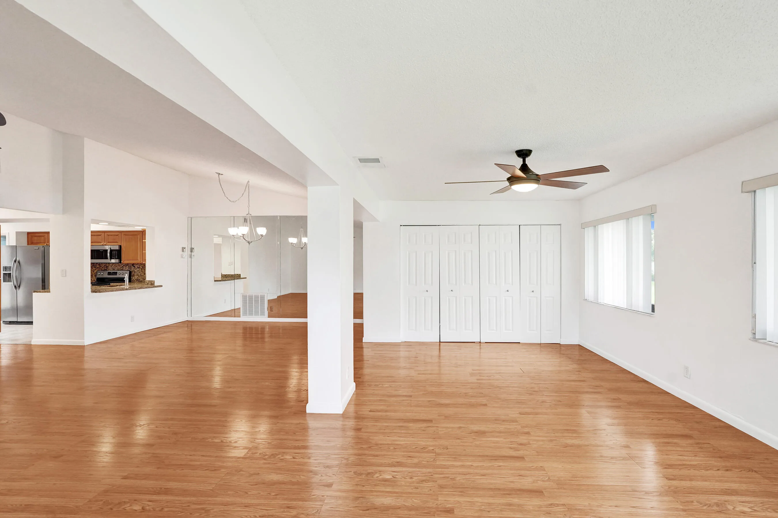 Expansive open-concept living area featuring wood-finish flooring, two windows with blinds, and a ceiling fan