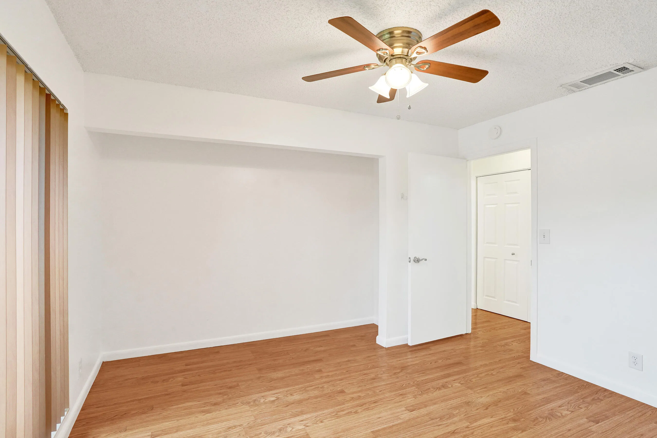 Wood-finish flooring, ceiling fan with integrated lighting, and a white interior door