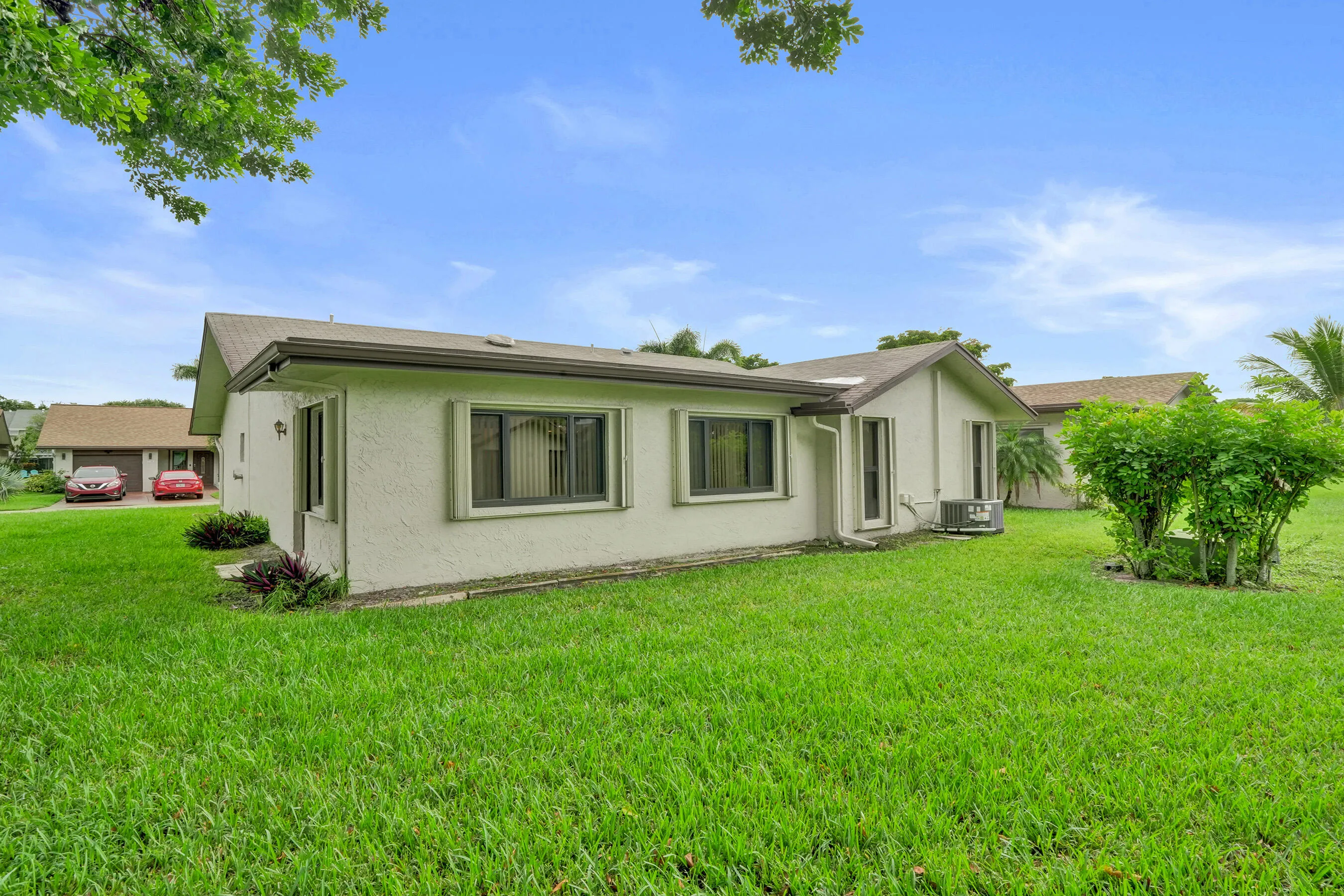 Expansive lawn space surrounding the property, featuring a stucco exterior, brown shingle roof, and multiple windows